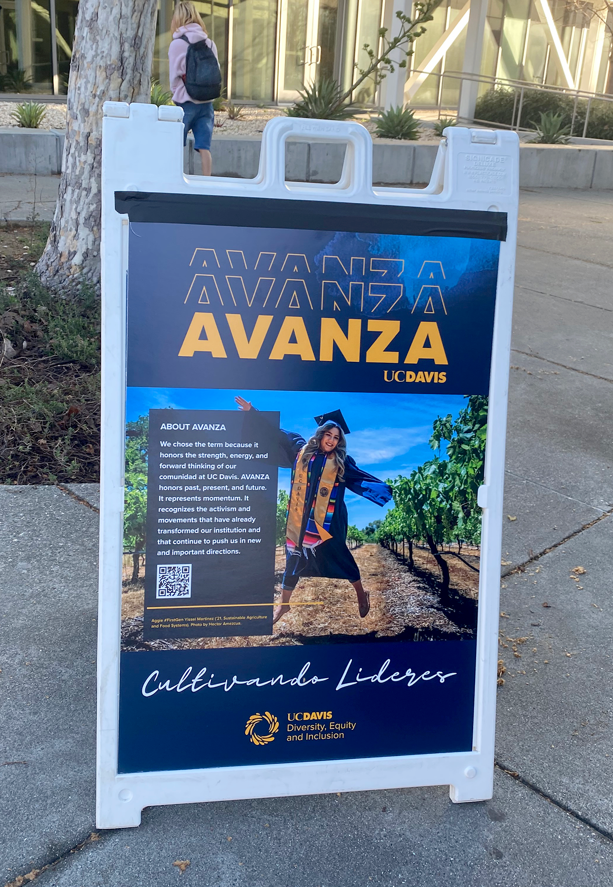 A poster on a board with an image of a female graduate student jumping and the words "AVANZA: cultivando líderes."