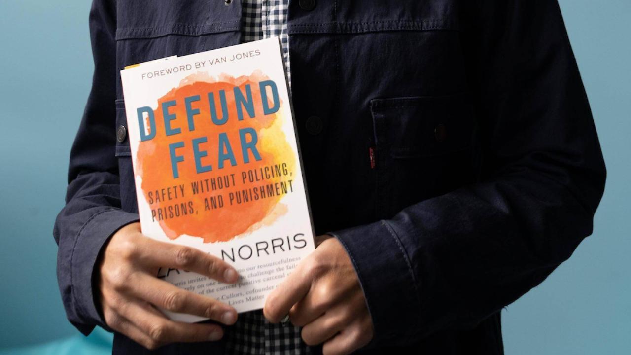 black hands holding a copy of the book "defund fear"